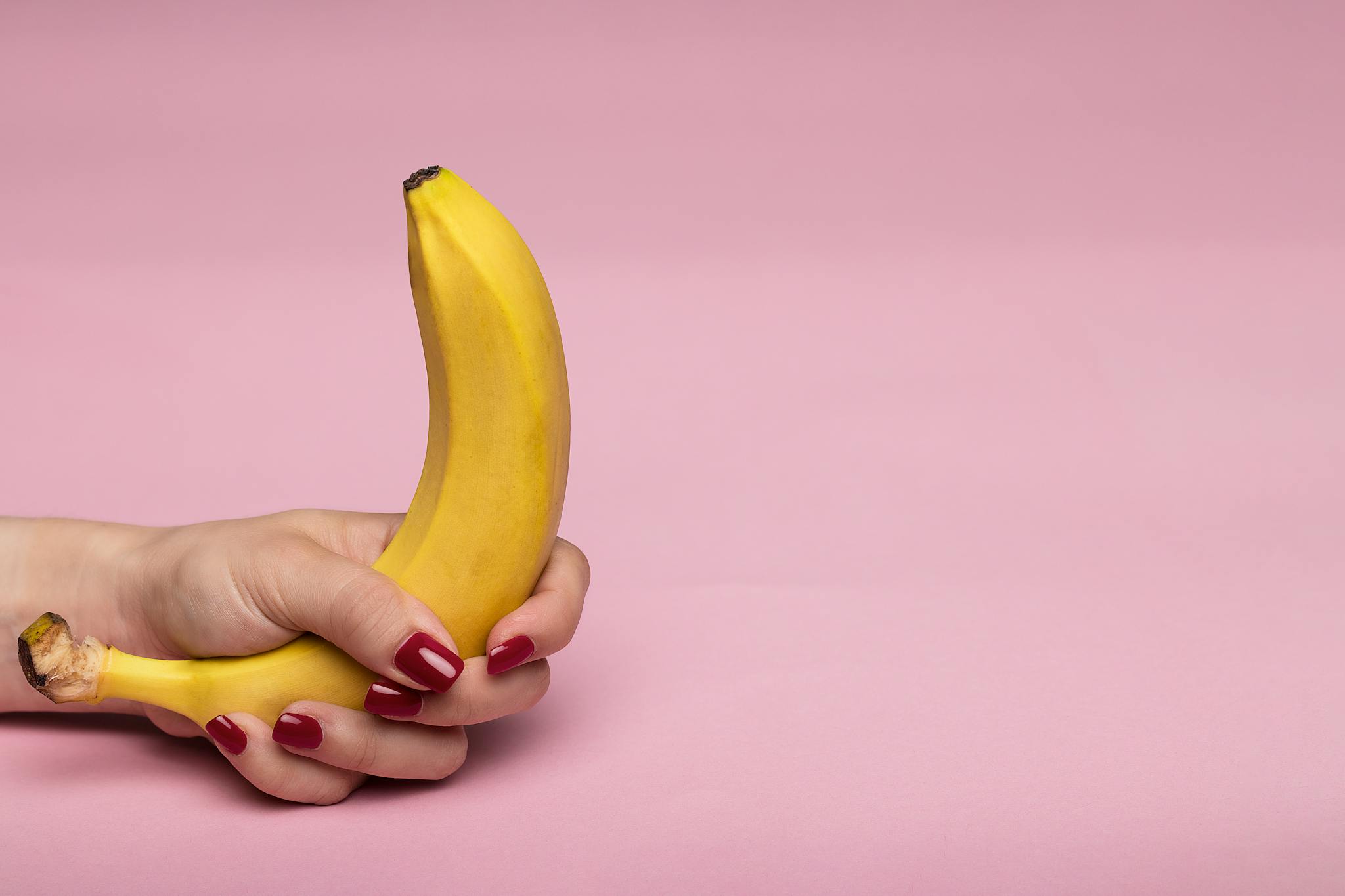 Close-up of a hand holding a banana on a pink background, highlighting conceptual and artistic themes.