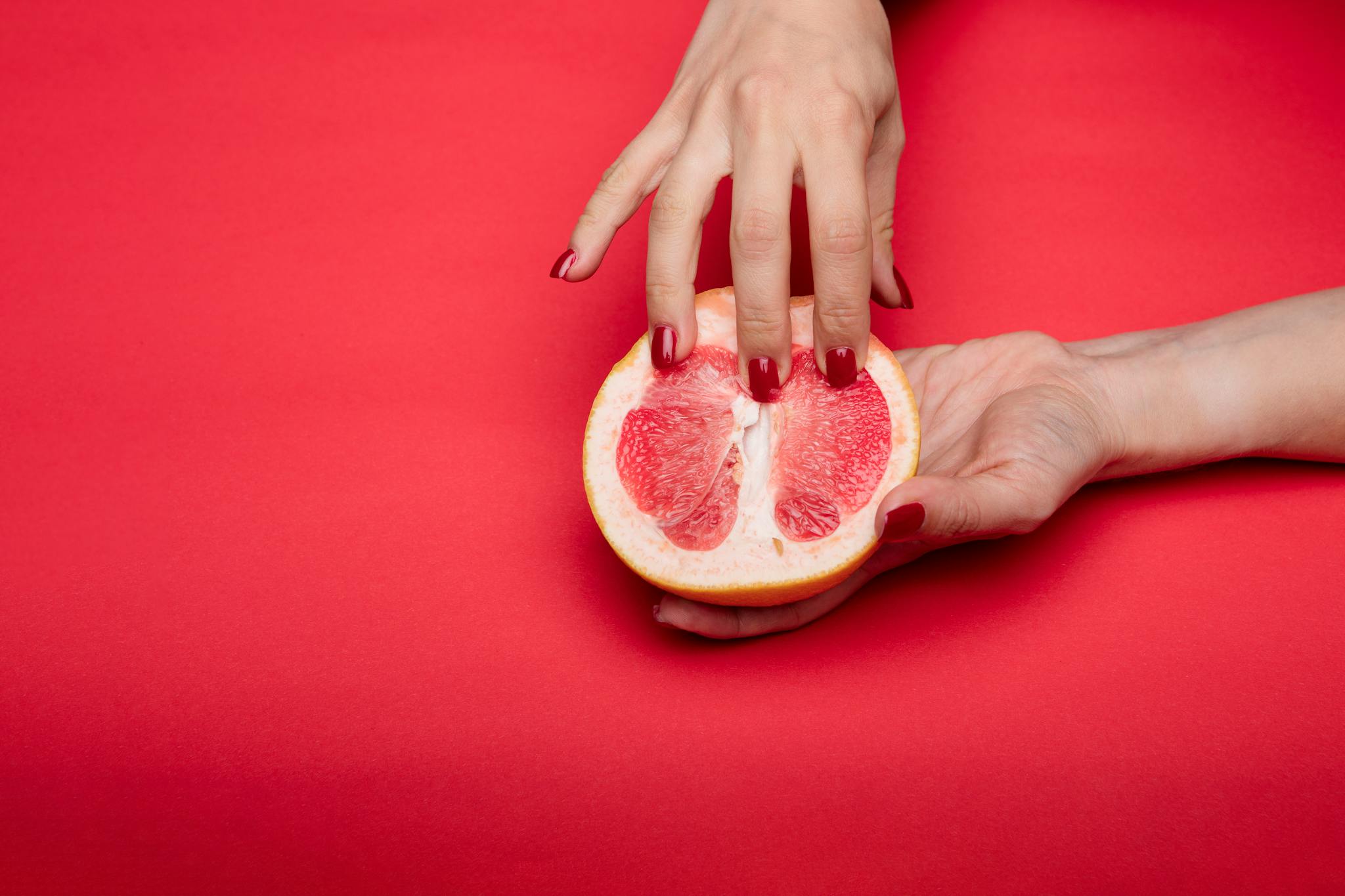 Creative close-up of hands holding grapefruit on red background, symbolizing femininity.